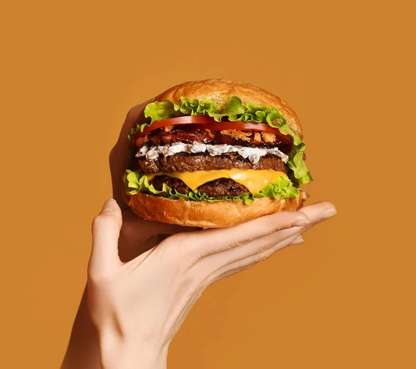 Kobieta ręce trzymać duże dwukrotnie cheeseburger sandwich burger z wołowiny i boczek na żółty — Zdjęcie stockowe