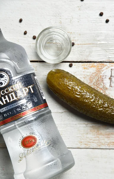 Een borrel wodka en een fles wodka liggen bij de gepekelde komkommer op tafel. Stockfoto