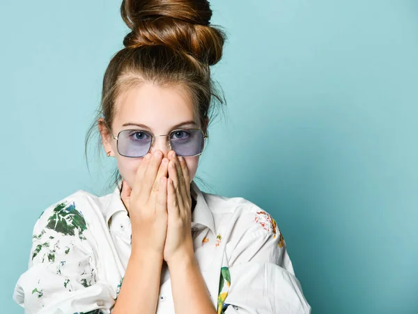 Retrato de una joven en camisa blanca con manchas de pintura y gafas translúcidas que cubren su boca con las manos — Foto de Stock