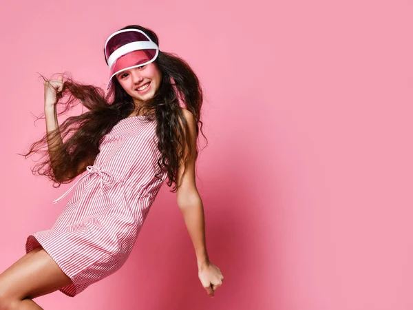 美しいですティーン女の子でAキャップとピンクの縞模様のドレス楽しいショーA勝者サイン笑い運上のピンクの背景 — ストック写真