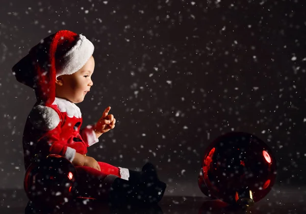 Mały chłopiec w stroju Świętego Mikołaja i kapelusz jeździ drewnianym koniem dla dzieci huśtawka z pudełkami noworocznych prezentów — Zdjęcie stockowe