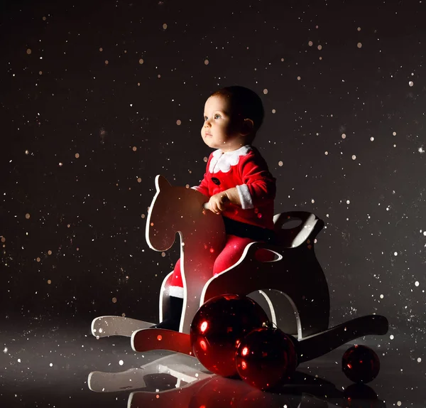 Μικρό παιδί αγόρι σε κοστούμι Άγιος Βασίλης και καπέλο βόλτες με ένα ξύλινο άλογο για τα παιδιά swing με το νέο έτος κουτιά δώρων — Φωτογραφία Αρχείου