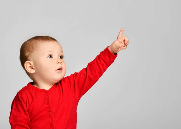 Kleine peuter jongen wijst vinger omhoog kant in rode baby bodysuit met vrije tekstruimte op grijs — Stockfoto