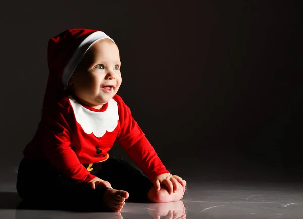 Ευτυχισμένος χαμογελαστός ξυπόλυτος μωρό αγόρι σε κόκκινο καπέλο Χριστούγεννα και το νέο έτος κοστούμι κάθεται κοιτάζοντας χώρο αντίγραφο — Φωτογραφία Αρχείου