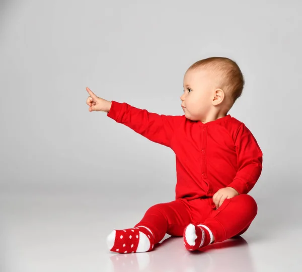 Little toddler boy points finger up side in red infant bodysuit with free text space on gray full body — Stock Photo, Image
