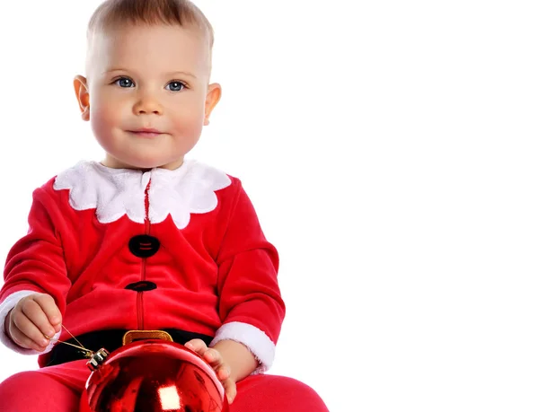 Noel Baba kostümü içinde küçük çocuk Noel Baba ve şapkalı mutlu bir gülümseme ile kırmızı hediye balosu köknar süslemesini kutlamaya hazır. — Stok fotoğraf