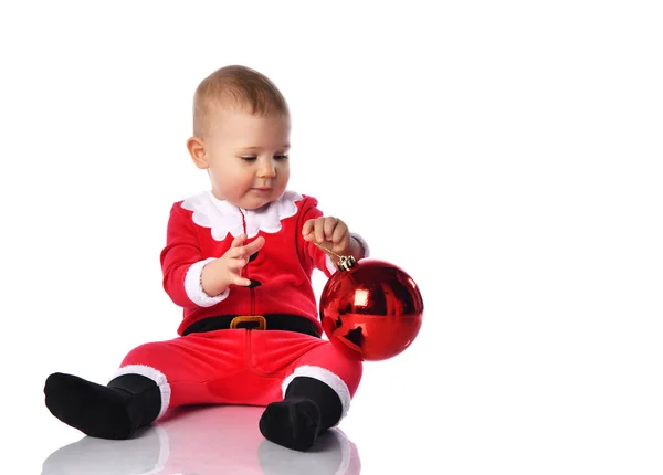 Noel Baba kostümü içinde küçük çocuk Noel Baba ve şapkalı mutlu bir gülümseme ile kırmızı hediye balosu köknar süslemesini kutlamaya hazır. — Stok fotoğraf