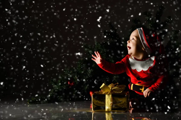 Barnebarn-gutt med blå øyne glad når han sitter i santa-hatt med gulljulegave – stockfoto