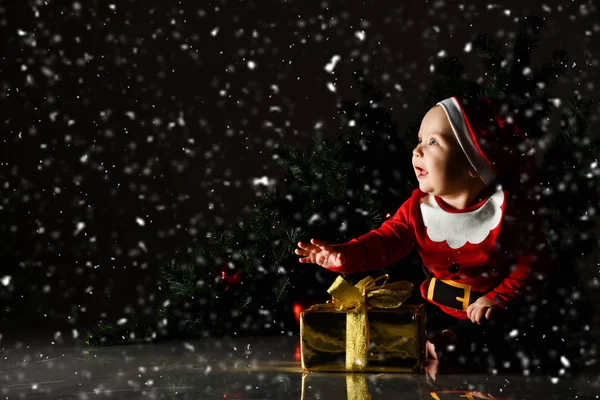 Niemowlę dziecko chłopiec dzieciak z niebieskimi oczami szczęśliwy uśmiech siedzi w kapeluszu Mikołaja ze złotym pudełku prezentów świątecznych — Zdjęcie stockowe