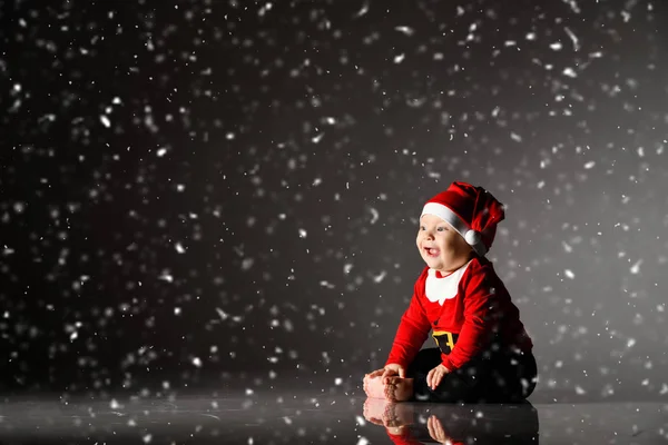Rire bébé enfant bébé garçon tout-petit est assis dans le costume de Père Noël claus et casquette sous la neige sur sombre avec espace de copie — Photo
