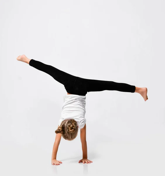 Athletic kid girl is doing gymnastic acrobatics exercises, handstand and stretching with her legs up on white — Stock Photo, Image