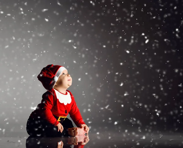 Bébé garçon souriant tout-petit est assis en costume de Père Noël claus et casquette sous la neige en regardant dans le coin à l'espace de copie — Photo