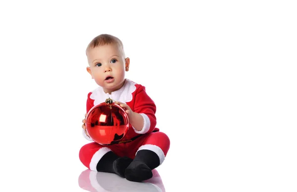 붉은 산타클로스 크리스마스 의상을 입은 작은 아기가 빨간 크리스마스 공 전나무 장식을 가지고 노는 모습 — 스톡 사진