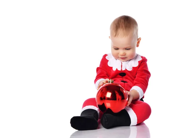 Lille guttebarn i Santa Clara-kostyme utforsker stadig å se på rødt juletre-ball-pynt – stockfoto