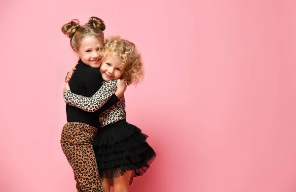 Two smiling kids girls best friends sisters in leopard print clothes pants and sweater are hugging feeling love on pink — Stock Photo, Image