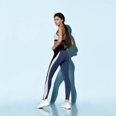 Spor kıyafetli güzel bir bayan açık mavi üzerinde spor egzersizleri yapıyor. 