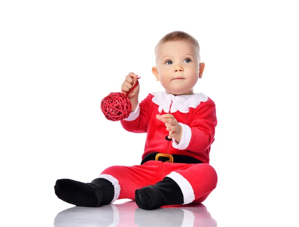 산타클로스 크리스마스 의상을 입고 모자를 쓰고 축하 할 준비가 되어 있는 빨간 선물 공 모양의 장식물로 행복하게 미소짓고 있는 어린 소년 — 스톡 사진