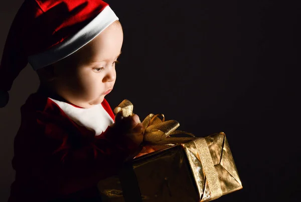 Portrait de bébé garçon tout-petit en costume de Noël rouge et casquette tenant l'ouverture de sa boîte cadeau nouvelle année cadeau — Photo