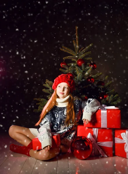 Mladá dívka sedící na oslavu zdobí vánoční stromek v červené zimní klobouk a dárky dárkové krabice. Nový rok Vánoce — Stock fotografie