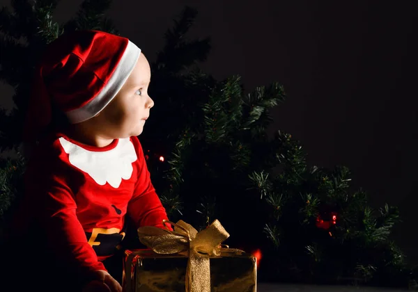 Noel Baba kostümlü bebek bebek bebek portresi Noel ağacı arka planında hediye kutusunu tutuyor. — Stok fotoğraf