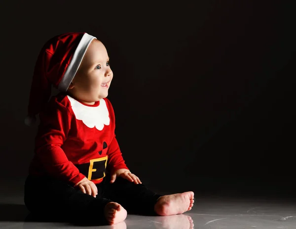 Mutlu gülümseyen bebek bebek bebek Noel Baba kostümü içinde oturmuş fotokopi çekerek karanlıkta ışık ışınlarına bakıyor. — Stok fotoğraf