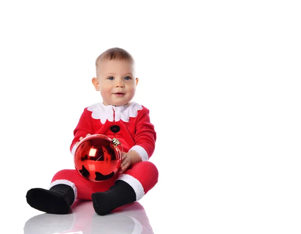 Mutlu gülümseyen küçük çocuk Noel Baba 'nın Noel Baba kostümünde kırmızı top köknar süslemesiyle oynuyor. — Stok fotoğraf