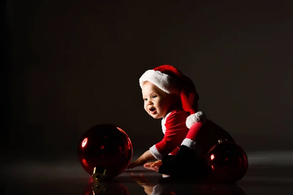 Incroyable bébé garçon tout-petit en costume de nouvel an rouge joue avec la décoration de l'arbre de Noël, roulement boule rouge sapin — Photo