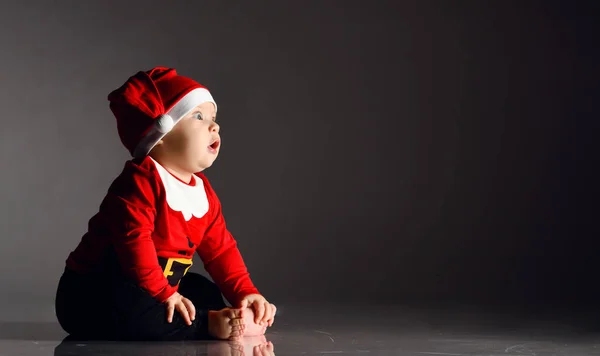 Yalınayak gezen çocuk çocuk çocuk. Kırmızı Noel Baba kostümüyle karanlıkta oturmuş fotokopi odasına bakıyor. — Stok fotoğraf