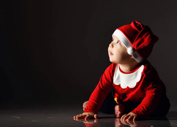 Souriant tout-petit garçon en costume de père Noël est assis commencer à ramper sur la glace en regardant dans le coin à l'espace de copie — Photo