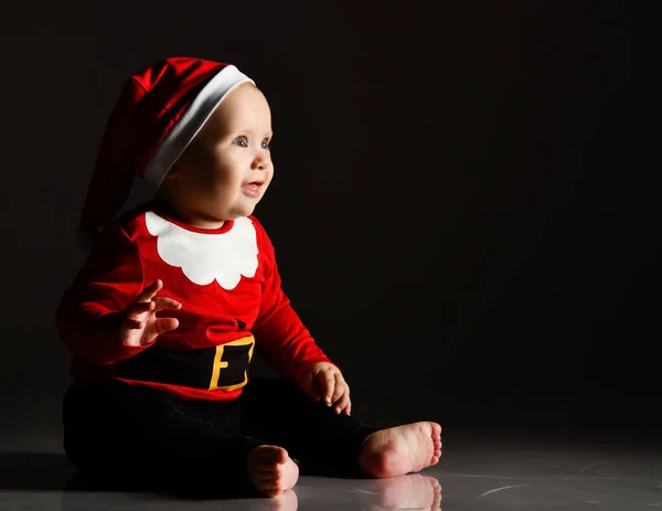 Büyüleyici bebek Noel Baba kostümünde oturmuş ışık ışınlarına bakıyor, koyu renk ışıkta el ele tutuşuyor. — Stok fotoğraf