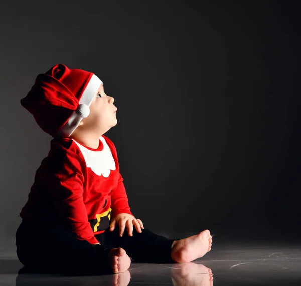 Calme bébé garçon tout-petit en costume santa claus est assis pieds nus sur la glace en regardant attentivement dans le coin à l'espace de copie — Photo