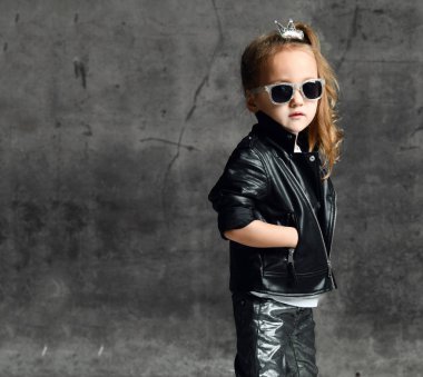 Deri ceketli, kot pantolonlu ve güneş gözlüklü havalı vahşi kız beton arka planda bir motorcu rock yıldızı gibi poz veriyor.