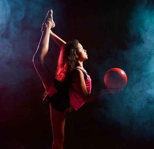 Νεαρή αδύνατη αθλήτρια γυμνάστρια που κάνει γυμναστικές ασκήσεις κατακόρυφη διατάσεις με μπάλα στο χέρι σε πιτσιλιές καπνού — Φωτογραφία Αρχείου