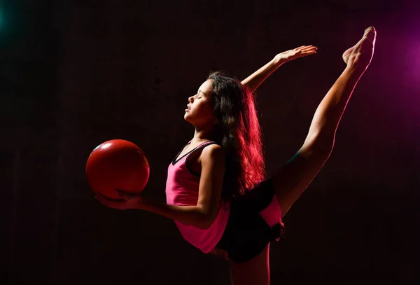 Giovane ragazza atletica sottile ginnasta facendo esercizi di ginnastica che si estende con la palla in mano in luci al neon — Foto Stock