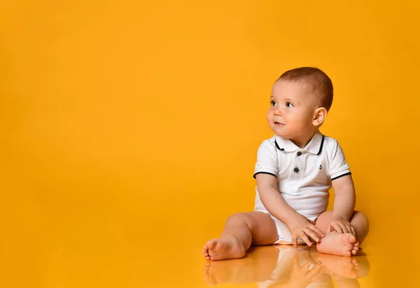 Glimlachende baby jongen peuter zit op de vloer te kijken opzij op gratis kopieerruimte op gele achtergrond — Stockfoto