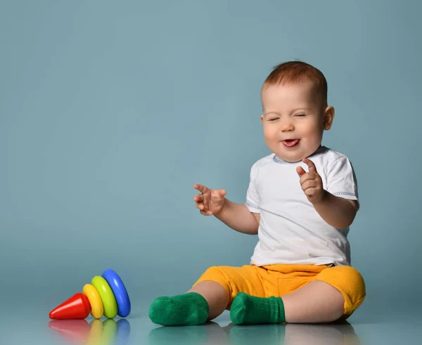 Éternuement riant Bébé garçon tout-petit joue avec un enfant multicolore pyramide en développement tombé sur le sol — Photo