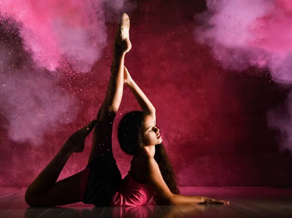 Молодая спортсменка гимнастка делает гимнастические упражнения, лежа на полу, держа ноги вверх, растягиваясь в дымовых залпах — стоковое фото