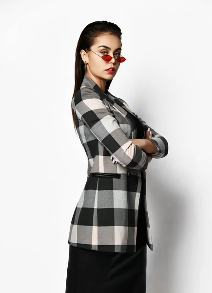 Young glamorous modern girl in a checkered jacket and black skirt wear red fashion glasses posing — ストック写真