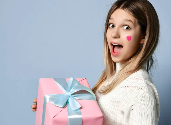 Улыбающаяся девочка-подросток празднует День Святого Валентина, держа большую розовую подарочную коробку на день рождения счастливый смех на светло-голубой — стоковое фото