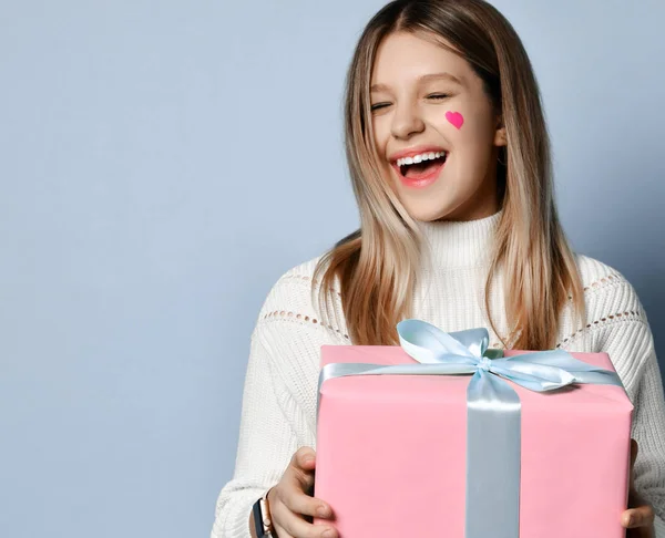 Smiling teen kid girl celebrate valentines day holding a big pink present gifts box for birthday happy laughing on light blue — ストック写真