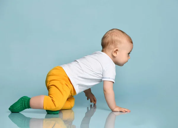Enfant bébé garçon enfant en pantalon jaune et t-shirt blanc rampant à quatre pattes sur fond bleu — Photo