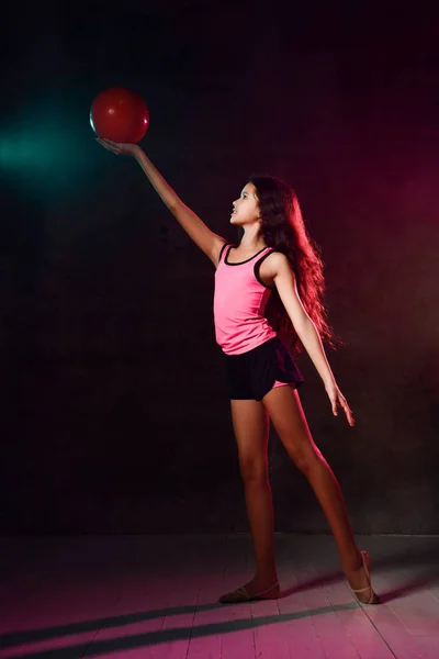 Uzun saçlı atletik kız jimnastikçi, jimnastik yapıyor, elinde kırmızı bir topla. — Stok fotoğraf