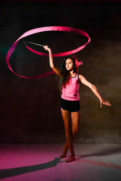 Slim teen girl with long curly hair is doing rhythmic gymnastic exercises with ribbon, doing circles over her head — Stock Photo, Image