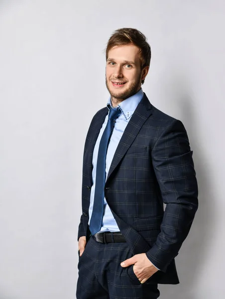Resmi kostüm ve kravatlı yakışıklı iş adamı açık gri duvarın üzerinde duruyor ve gülümsüyor. — Stok fotoğraf