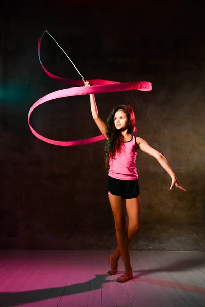 Slim dziewczyna nastolatek gimnastyczka z długimi włosami robi gimnastyka rytmiczna ćwiczenia z taśmą, rysunek krąg wokół niej — Zdjęcie stockowe