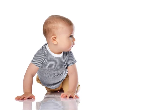 Infant child boy in t-shirt and green pants is crawling on all fours, looking aside at free copy space reading on white — Stock Photo, Image