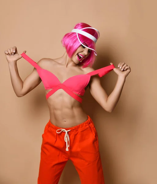 Jovem mulher magra positiva com cabelo rosa em sportswear brilhante de pé e sorrindo sobre fundo de parede amarelo — Fotografia de Stock