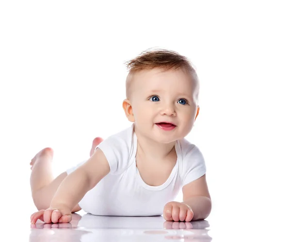 Happy smiling infant child baby boy toddler with blue eyes in white t-shirt is lying on his stomach crawling on white — 스톡 사진
