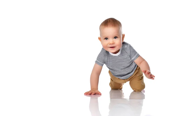 Happy and keen infant boy toddler in t-shirt and green pants is crawling on all fours on white with copy space — Stock Photo, Image