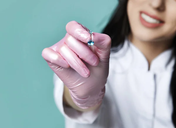 Closeup of young brunette woman cosmetologist in pink medical gloves handing us a jewellery for piercing — Stock Photo, Image